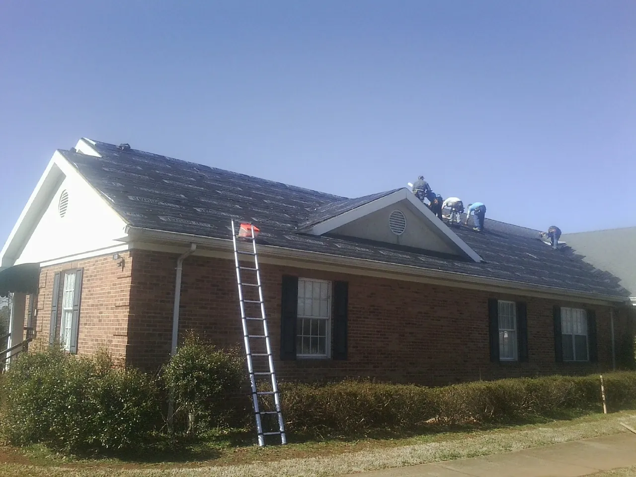 Crew tearing shingles off a brick ranch roof with a ladder set — Emergency Roof Repair work by our crew in Pasadena