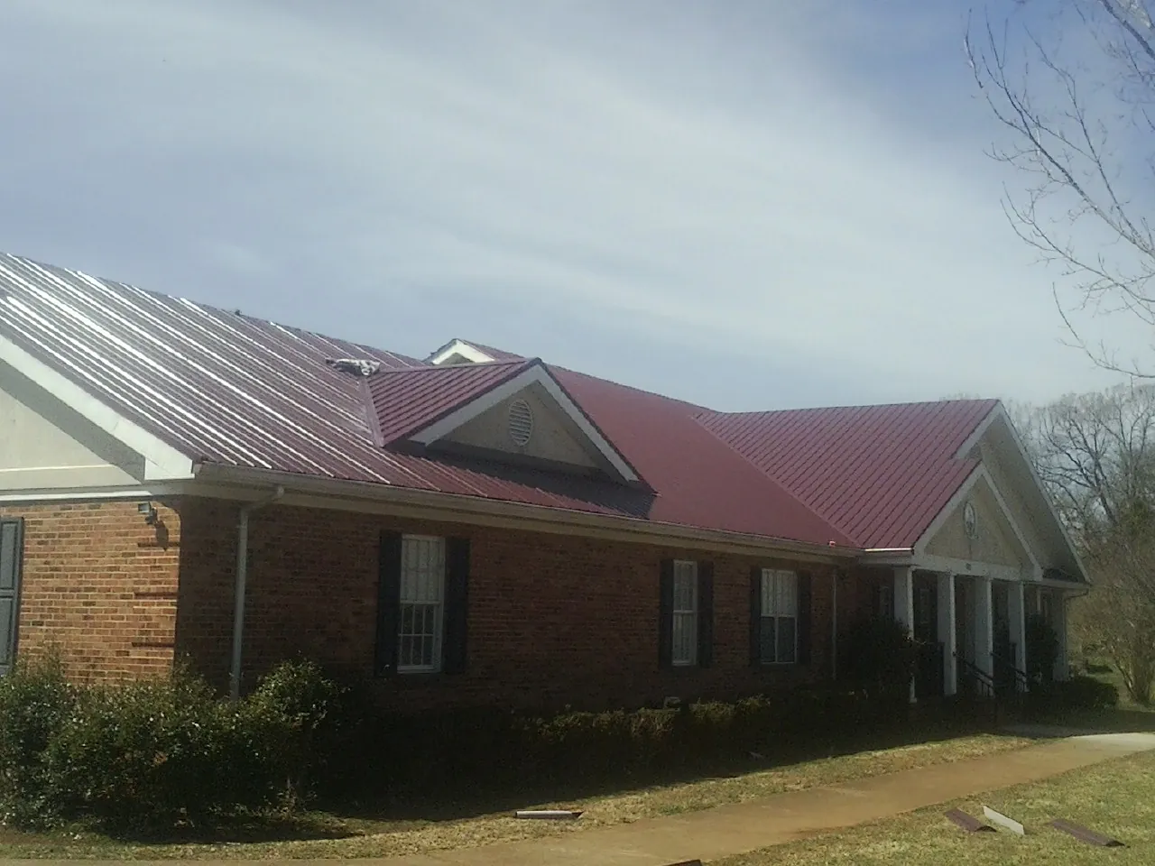 Red metal roof with gabled entries on a long brick building, from a Hail Damage Roof Repair job in Pasadena